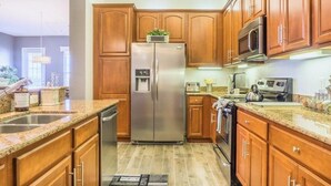 A kitchen with wooden cabinets, a stainless steel refrigerator, a microwave, and a dishwasher. - Lakeview Penthouse Elegance 3 Bedroom Condo by RedAwning (Orlando)