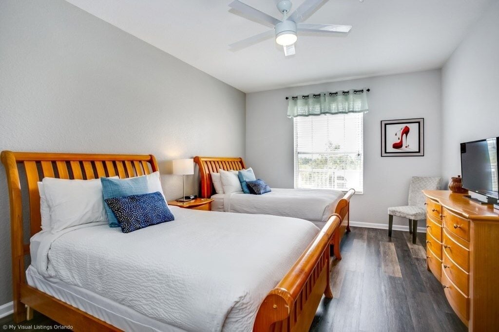 A bedroom with two wooden beds, a ceiling fan, a TV, and a window with a view.