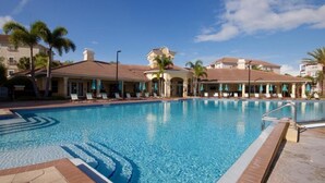 A swimming pool with lounge chairs and umbrellas, surrounded by buildings with a Mediterranean architectural style.