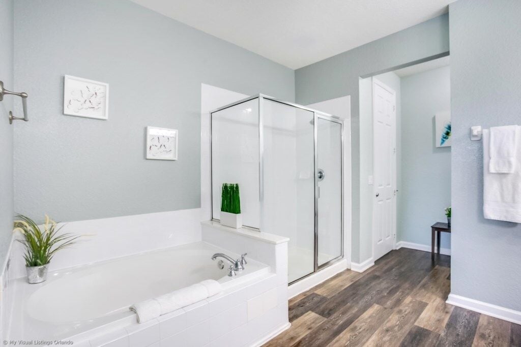 A modern bathroom with a large white bathtub, a glass-enclosed shower, and a wooden floor.