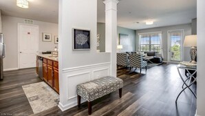 A modern kitchen with wooden cabinets, a built-in island, and a bench. There is a dining area with a table and chairs, and a living room with a sofa and a coffee table.