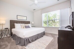A bedroom with a large bed, a ceiling fan, a window with blinds, a desk, and a lamp. - Vista Cay Casa Bonita 3 Bedroom Townhouse by RedAwning (Orlando)