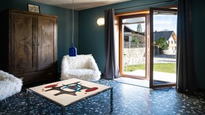 Una habitación con un armario de madera, una butaca blanca de pelo, una mesa con diseño rojo y azul, y una puerta de cristal que da al exterior.