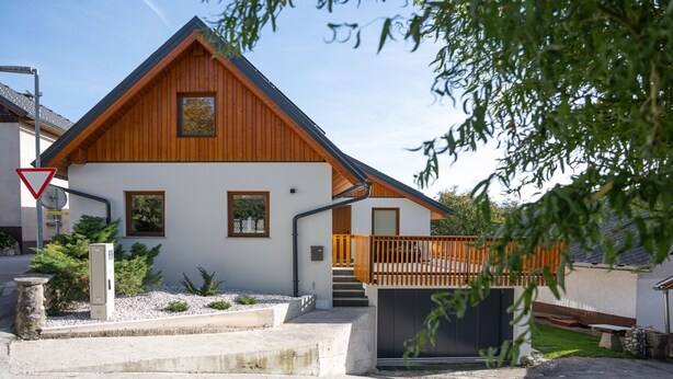 Una casa moderna de dos pisos con fachada de madera, un balcón y una escalera visible que lleva a la entrada.