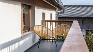 Un balcón con dos sillas de mimbre y una mesa de madera.