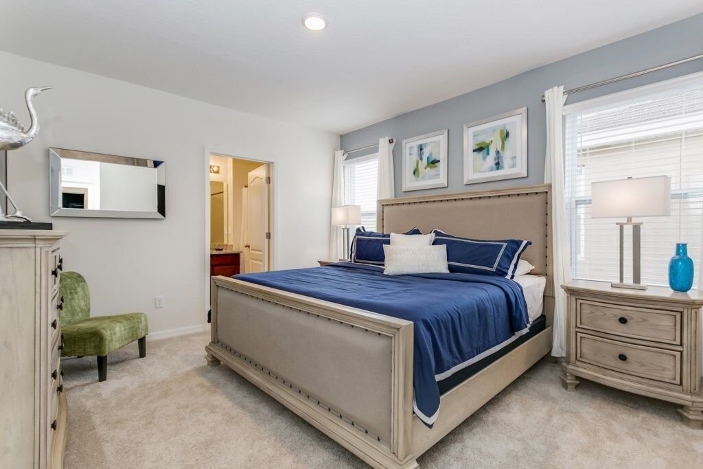 A bedroom with a large bed, a dresser, a chair, and artwork on the walls.