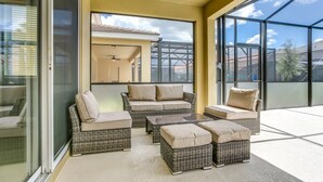 Un balcon ensoleillé, doté de meubles en osier, notamment d’un canapé et de plusieurs poufs, et une porte vitrée donnant sur un espace patio.