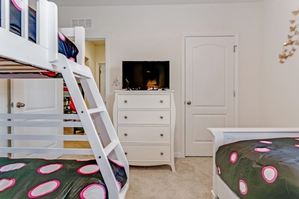 Un lit superposé pour enfant avec une échelle, une commode avec des tiroirs et un lit recouvert d’une couvre-lit à motifs verts et roses.