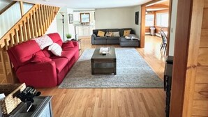 A spacious living room with a wooden staircase, a red sofa, a grey sofa, and a coffee table.