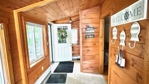 A wooden hallway with a 'WELCOME' sign, a door with a wreath, and a 'Welcome' sign with hanging items.