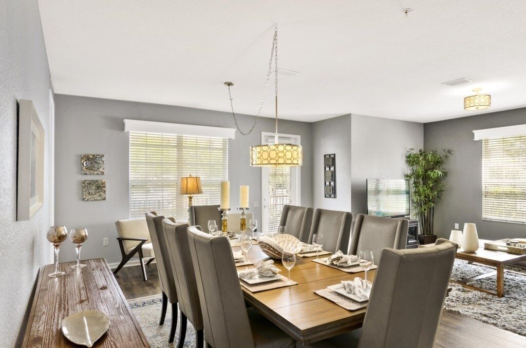 A dining area with a wooden table set for six, surrounded by chairs, and a hanging light fixture above.
