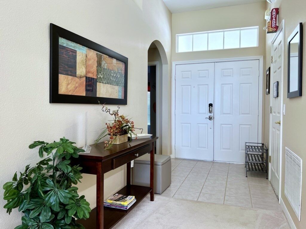 A hallway with a framed abstract painting, a potted plant, a small table with a vase, and a double door.