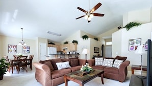 A living room with a brown sectional sofa, a wooden coffee table, a ceiling fan, and a television.