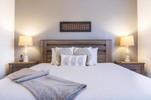A neatly made bed with a grey blanket, two bedside lamps, and a wooden headboard with decorative pillows.