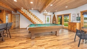 Interior de madera con mesa de billar, escalera y comedor.