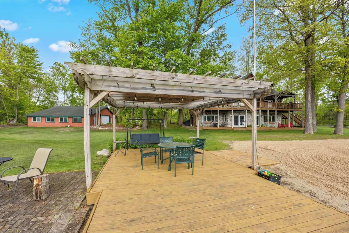 Eine Terrasse im Freien mit einer Holz-Pergola, einem Tisch mit Stühlen und einer Rasenfläche.