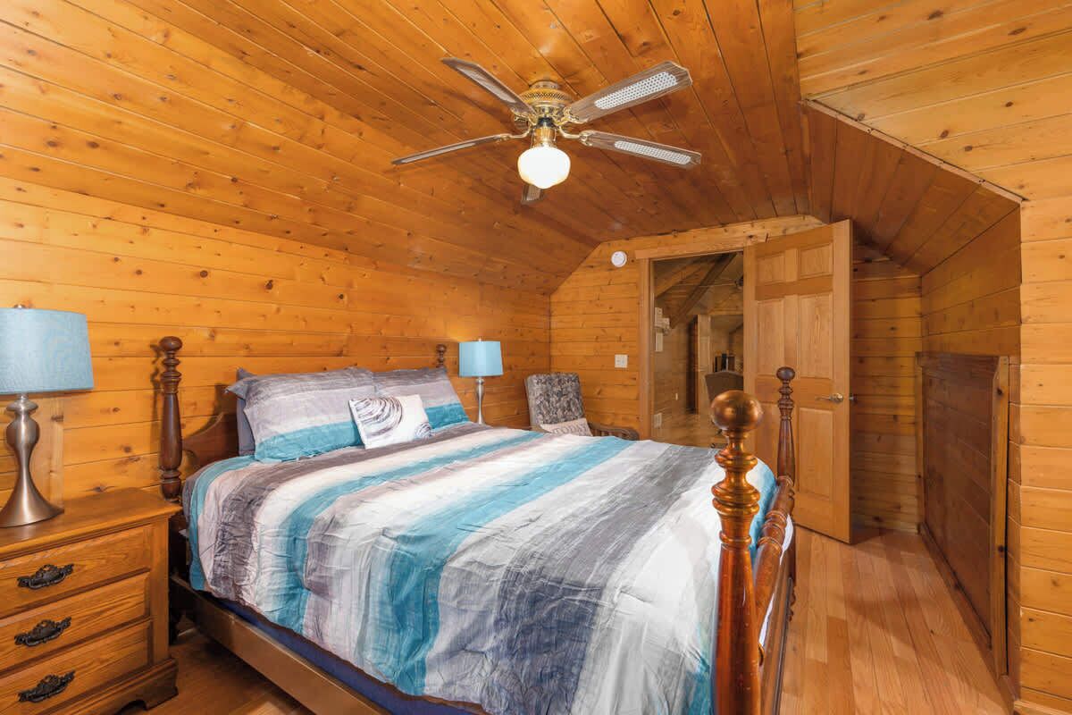 Une chambre à coucher dans une cabane en bois, comprenant un lit, des tables de chevet, un ventilateur de plafond et une porte donnant sur une autre pièce.