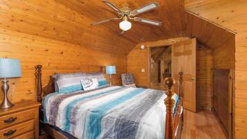 Une chambre à coucher dans une cabane en bois, comprenant un lit, des tables de chevet, un ventilateur de plafond et une porte donnant sur une autre pièce.