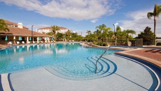 A swimming pool with lounge chairs and umbrellas, surrounded by palm trees and buildings. - Penthouse Utopia 3 Bedroom Condo by RedAwning (Orlando)