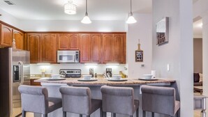 A modern kitchen with wooden cabinets, a central island with bar stools, stainless steel appliances, and pendant lighting. - Penthouse Utopia 3 Bedroom Condo by RedAwning (Orlando)
