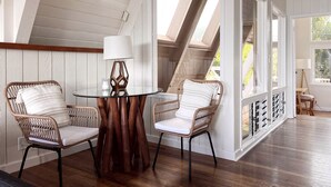 Ein Zimmer mit einem runden Glastisch, zwei Korbstühlen, einer weißen Lampe und Blick durch ein großes Fenster.