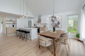 A modern kitchen with a central island, bar stools, pendant lighting, and a dining area with a wooden table and chairs.