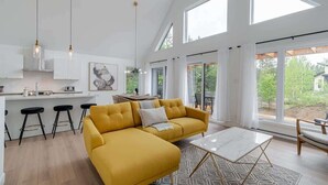 Et moderne køkken med barstole, en gul sofa og et spiseområde med udsigt til det fri.