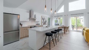 Et moderne køkken med en central ø, barstole og et spiseområde med en gul sofa.