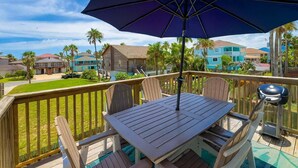 A wooden deck with a table and chairs, a large umbrella, and a barbecue grill. - Sun Dancer #11 2 Bedroom Home by RedAwning (South Padre Island)