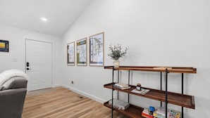 Un salon moderne avec un plancher en bois, un canapé gris, une porte blanche et une console en bois sur laquelle sont posés des livres et une plante.