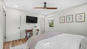 Une chambre à coucher comprenant un lit, un bureau, un téléviseur et des œuvres d’art encadrées accrochées au mur.