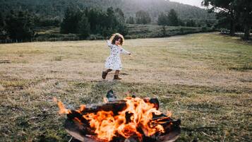 A child playing near a campfire in a grassy field with trees in the background.
