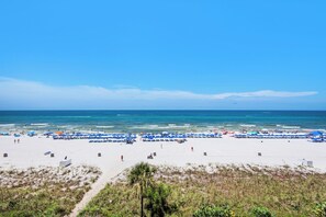 Ein Strand mit weißem Sand und blauen Sonnenschirmen, einem klaren Himmel und ruhiger See.