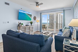 Una sala de estar con un ventanal grande, un ventilador de techo y vistas a un edificio de gran altura.