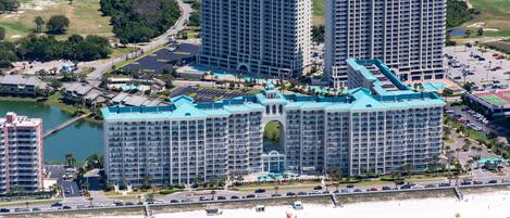 A large hotel complex with multiple high-rise buildings, a beachfront, and a golf course in the background.