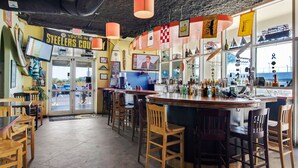 A bar area with wooden chairs, a counter with bottles, and a television screen.