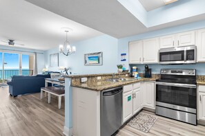 A modern kitchen with stainless steel appliances, a dining area with a view, and a living room with a balcony. - ⭐By Beach in Seascape-Gulf Views-2 Pools + Kids Fountain-2BR Ariel Dunes I 803 (Miramar Beach)