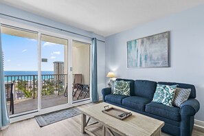 A living room with a sofa, coffee table, and a view of the ocean through a sliding glass door.