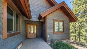 Una cabaña de madera con porche cubierto, ventanas amplias y entorno natural.