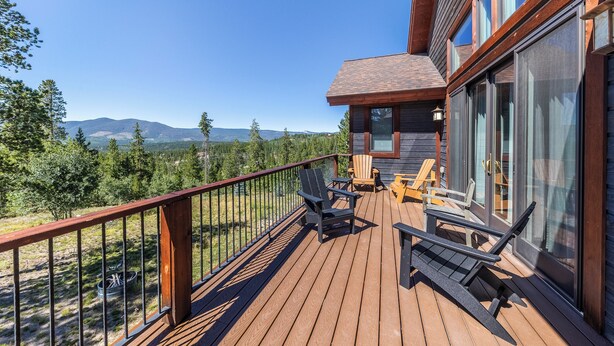 Terraza de madera con mobiliario exterior y vistas a montañas.