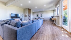 Amplia sala de estar con un sofá modular grande, un televisor de pantalla plana y una mesa de comedor con sillas.