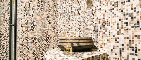 A bathroom with mosaic tile walls and a central basin with a decorative item.