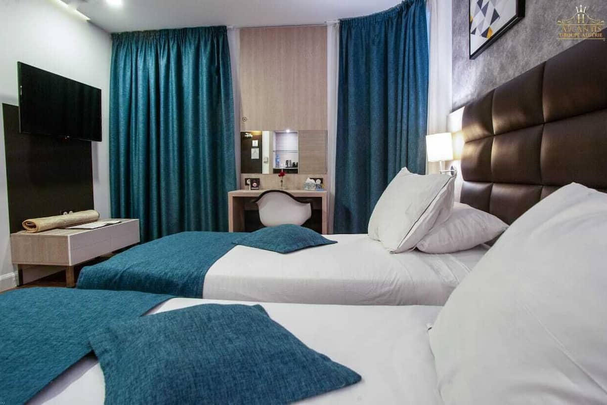 A hotel room with two beds, a flat-screen TV, a desk with a lamp, and a large mirror.