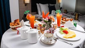 A breakfast table set with croissants, orange juice, a fruit salad, and a plate with eggs and vegetables.