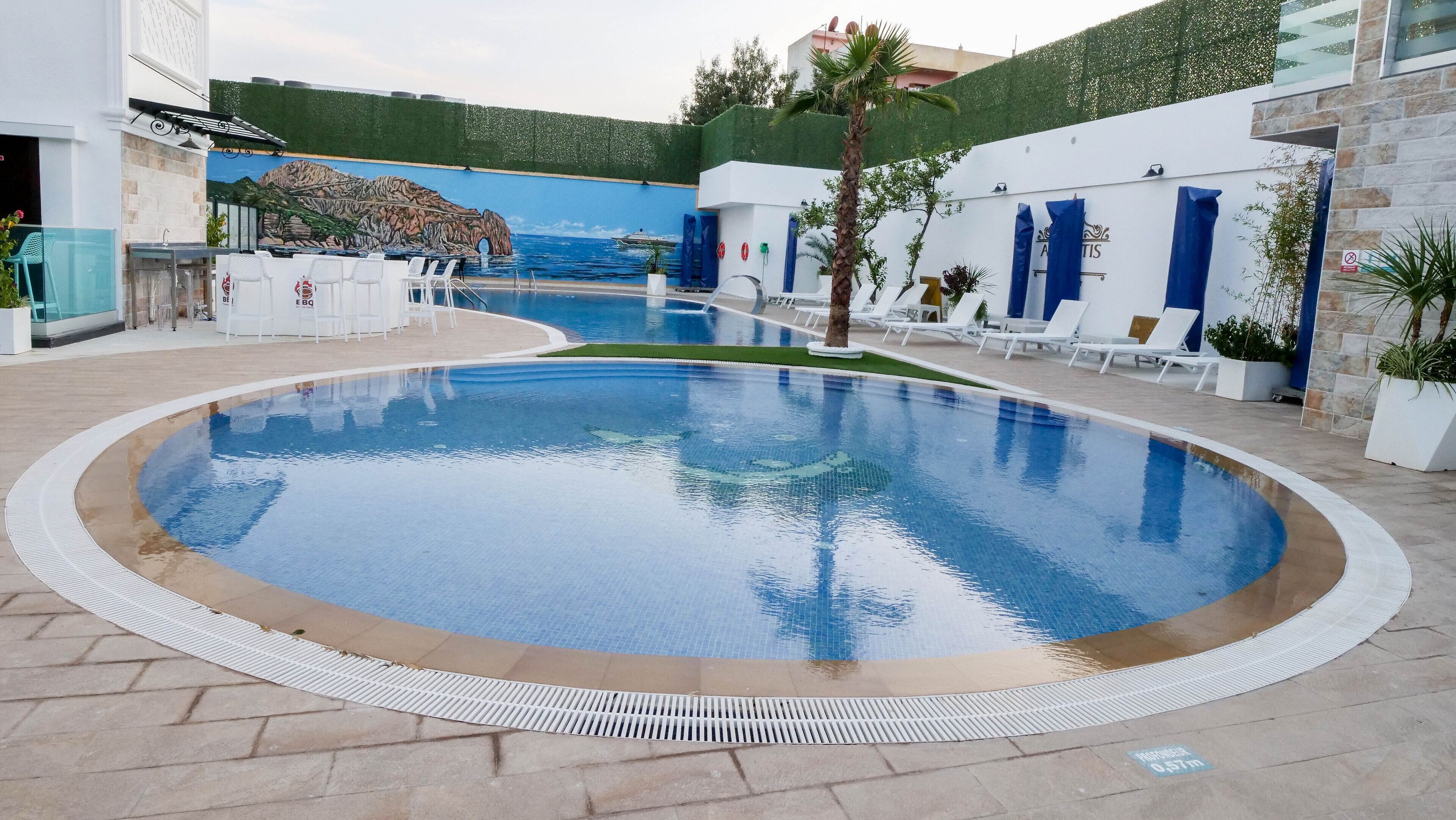 A swimming pool with a mural backdrop, lounge chairs, and a BBQ area.