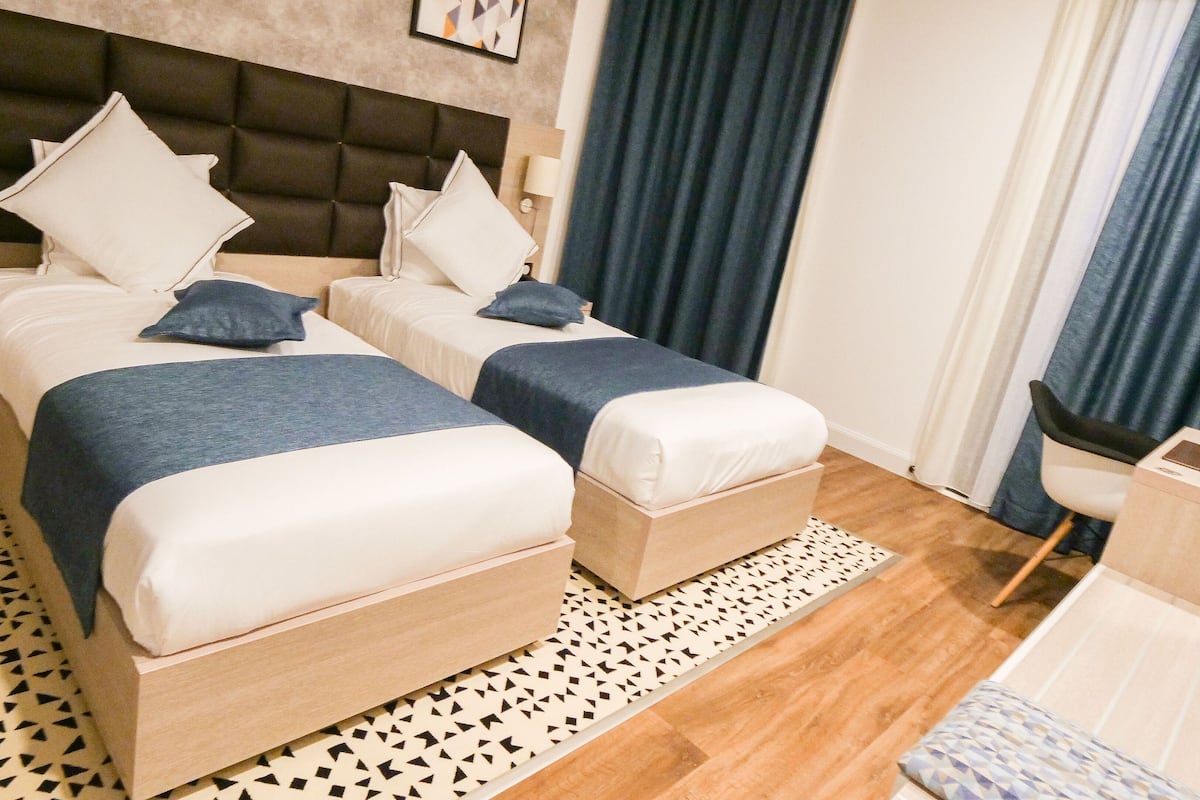A hotel room with two beds, a nightstand, a desk, and a chair.