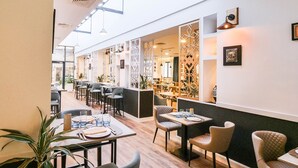 A modern restaurant with a long counter, multiple tables, and chairs. There are decorative wall panels and pendant lighting.