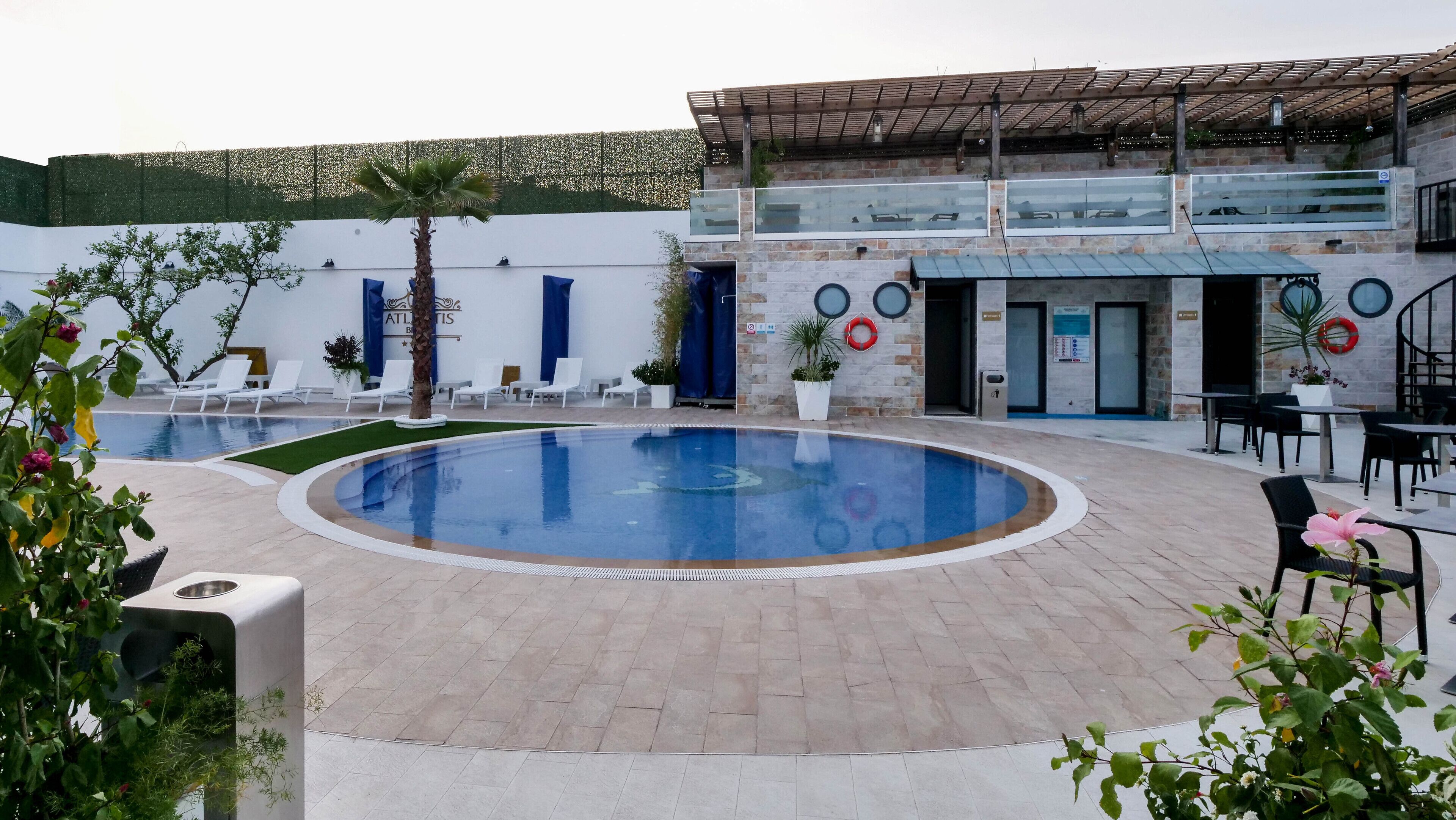 A pool area with lounge chairs, a covered seating area, and a building with a stone facade.