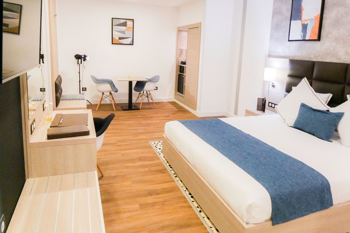 A hotel room with a bed, a desk, a chair, a small table, and a TV.