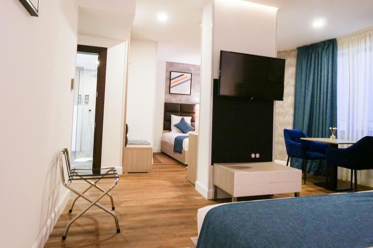 A modern hotel room with a bed, a TV, a desk, and a chair. There is a bathroom visible in the background.
